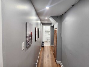 A hallway with grey walls, wooden flooring, and a door leading to a bathroom.