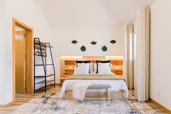 A bedroom with a bed, a bench, a wooden wardrobe, a shelf unit, and a wall-mounted plant. - Casa Ti'Vina - North Side (Caniço)