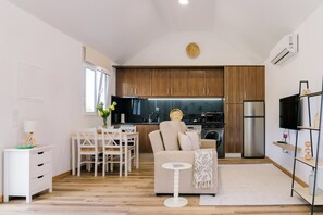 A modern kitchen with wooden cabinets, a stainless steel refrigerator, and a dining area with a white table and chairs. - Casa Ti'Vina - North Side (Caniço)