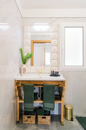 A bathroom with a white sink, wooden vanity, green towels, a potted plant, and a gold trash can. - Casa Ti'Vina - North Side (Caniço)