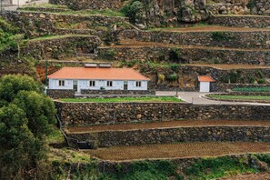 A white building with a red roof, surrounded by stone terraces and greenery. - Casa Ti'Vina - North Side (Caniço)