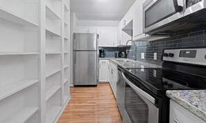 Eine moderne Küche mit weißen Schränken, einem Edelstahl-Kühlschrank, einer schwarzen Arbeitsplatte und einer schwarzen Fliesenwand.