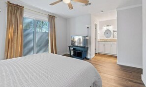 Ein Schlafzimmer mit Bett, Vorhängen, Deckenventilator, Fernseher und einem Badezimmer mit Spiegel und Waschbecken.