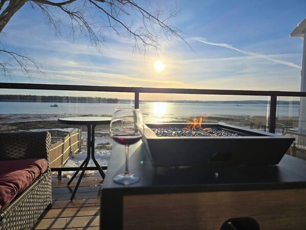 Ein Balkon mit Tisch, einem Glas Rotwein und einem Grill mit Blick auf ein Gewässer.