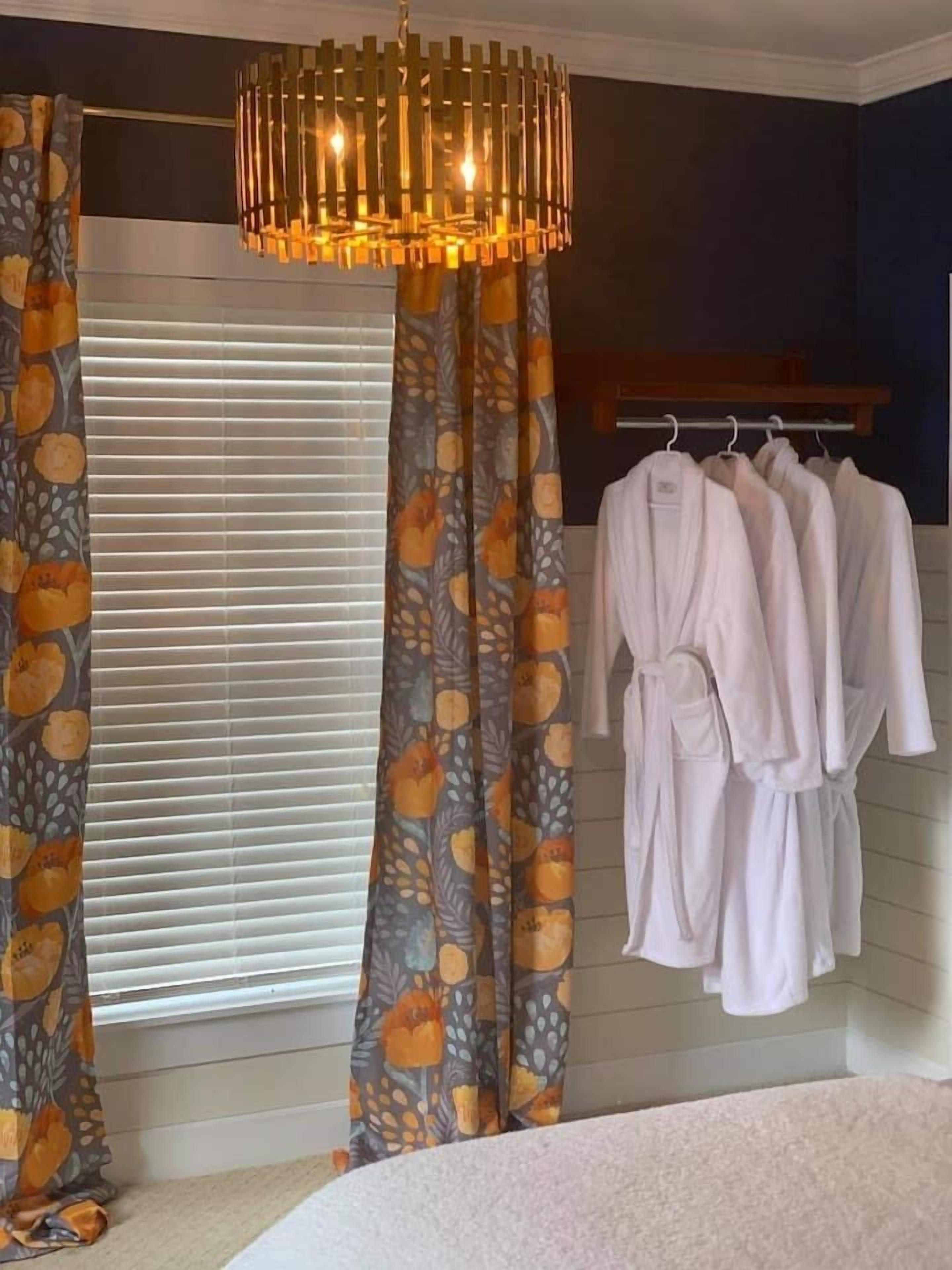 Une chambre à coucher comprenant un lit, une fenêtre avec des stores, un rideau à motifs, un porte-vêtements suspendu et un luminaire suspendu.