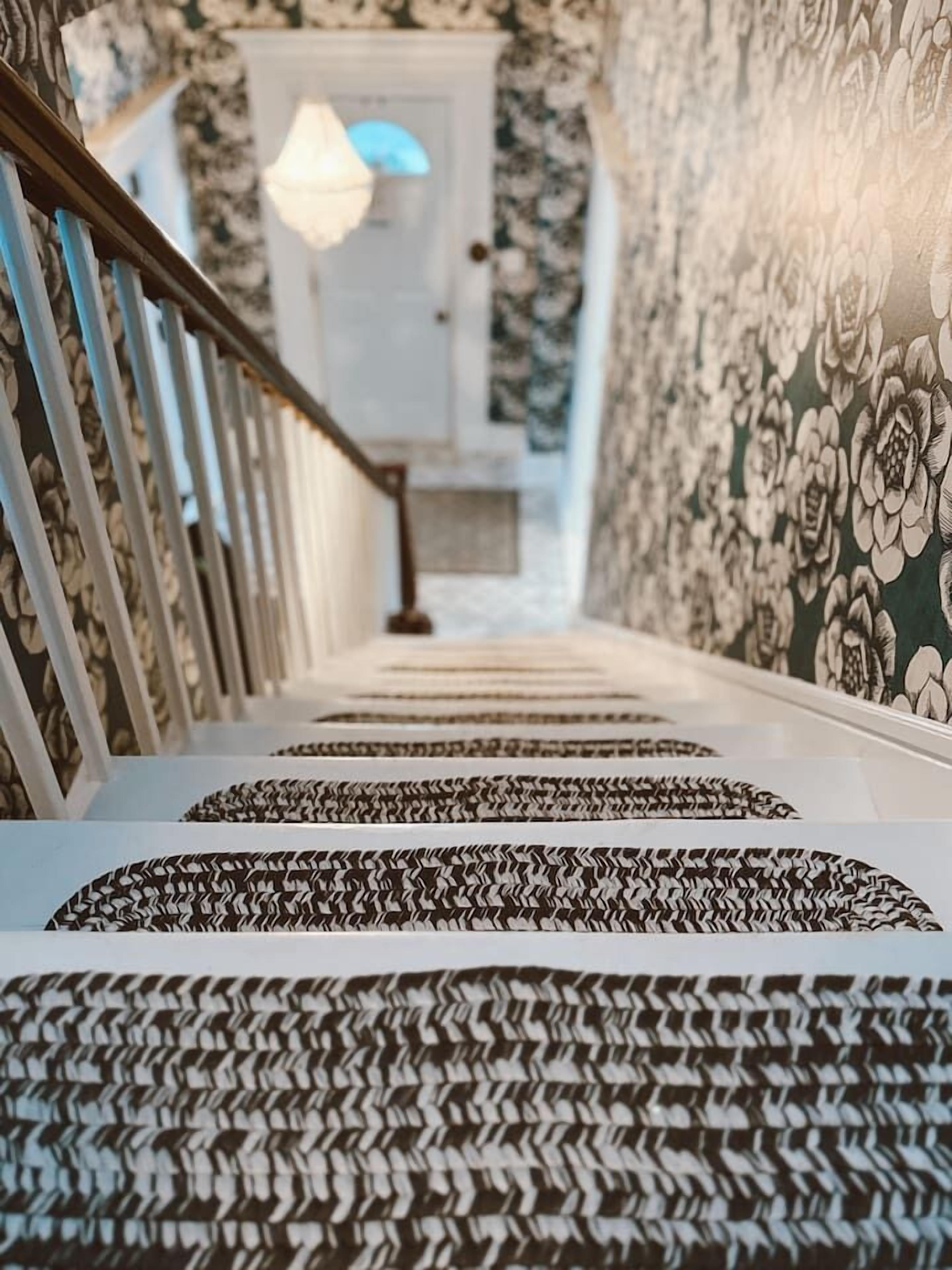 A staircase with patterned carpet and a railing, leading to a room with a door and a light fixture.