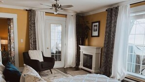 A bedroom with a bed, a chair, a fireplace, and a view of the outdoors.