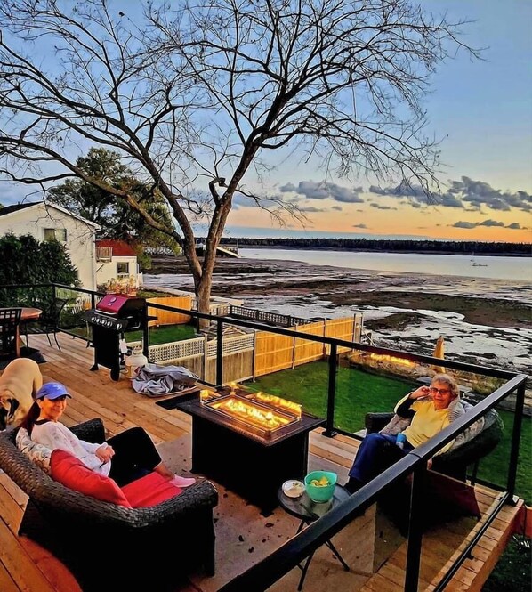 Um terraço com área de estar ao ar livre, churrasqueira e vista para a água.
