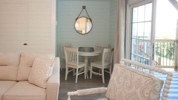Una habitación con un sofá blanco, un sillón estampado, una mesa de comedor con sillas y un espejo redondo en la pared.