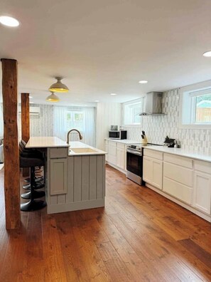 Una cocina moderna con una isla central, suelo de madera, armarios blancos y un ventanal que proporciona luz natural.
