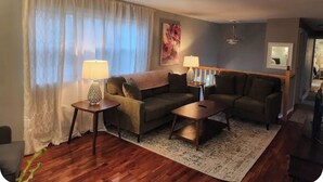Un salon avec un canapé, deux tables d’appoint, une lampe, un tapis et un tableau accroché au mur.