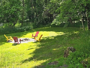 A grassy outdoor area with a fire pit and several Adirondack chairs. - The Heron's Perch - HL (Hampton)