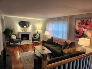 Un salon avec une cheminée, deux fauteuils, un canapé, une table basse et un téléviseur.
