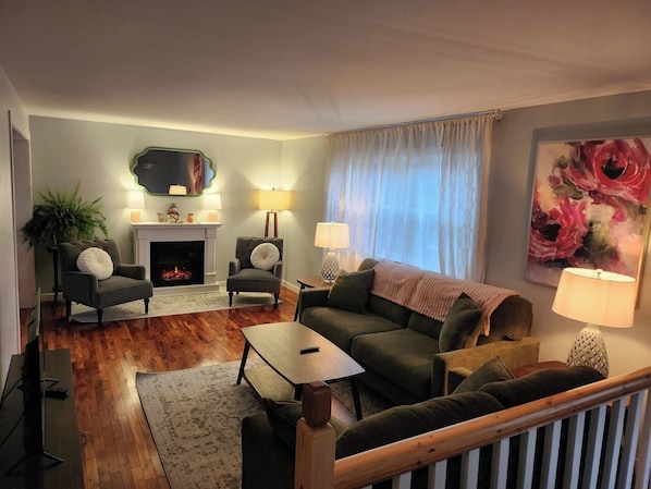 A living room with a fireplace, two armchairs, a sofa, a coffee table, and a TV. - The Heron's Perch - HL (Hampton)