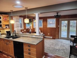 A kitchen with wooden cabinets, a built-in dishwasher, pendant lights, and a large island.