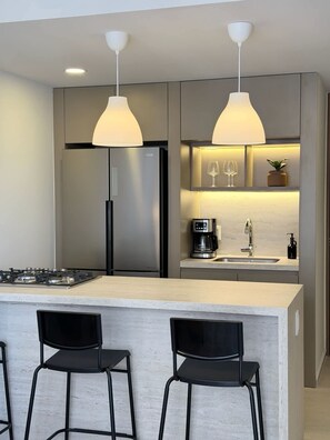 A modern kitchen with a central island, bar stools, a refrigerator, a coffee maker, and pendant lighting. - Apartment with city view in Zapopan, Jalisco (Zapopan)