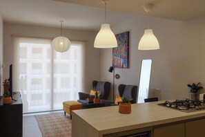 Eine moderne Küche mit einer zentralen Kochinsel, Pendelleuchten und einem Essbereich mit Stühlen und einer Couch.