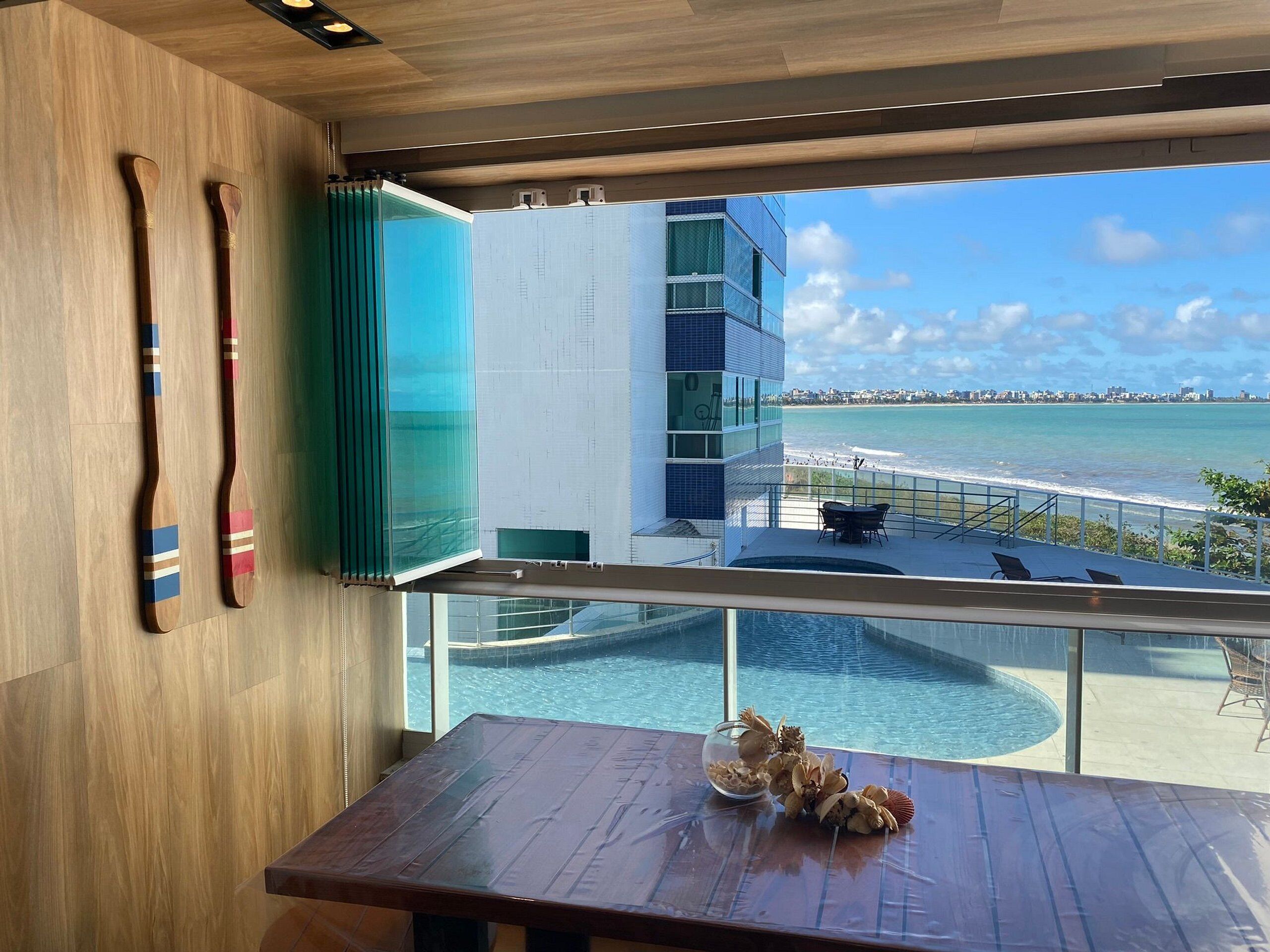 A modern room with a view of a pool and beach, wooden furniture, and a glass partition.