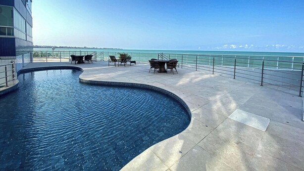 Una piscina con bordo curvo, area relax all'aperto e vista sull'oceano.