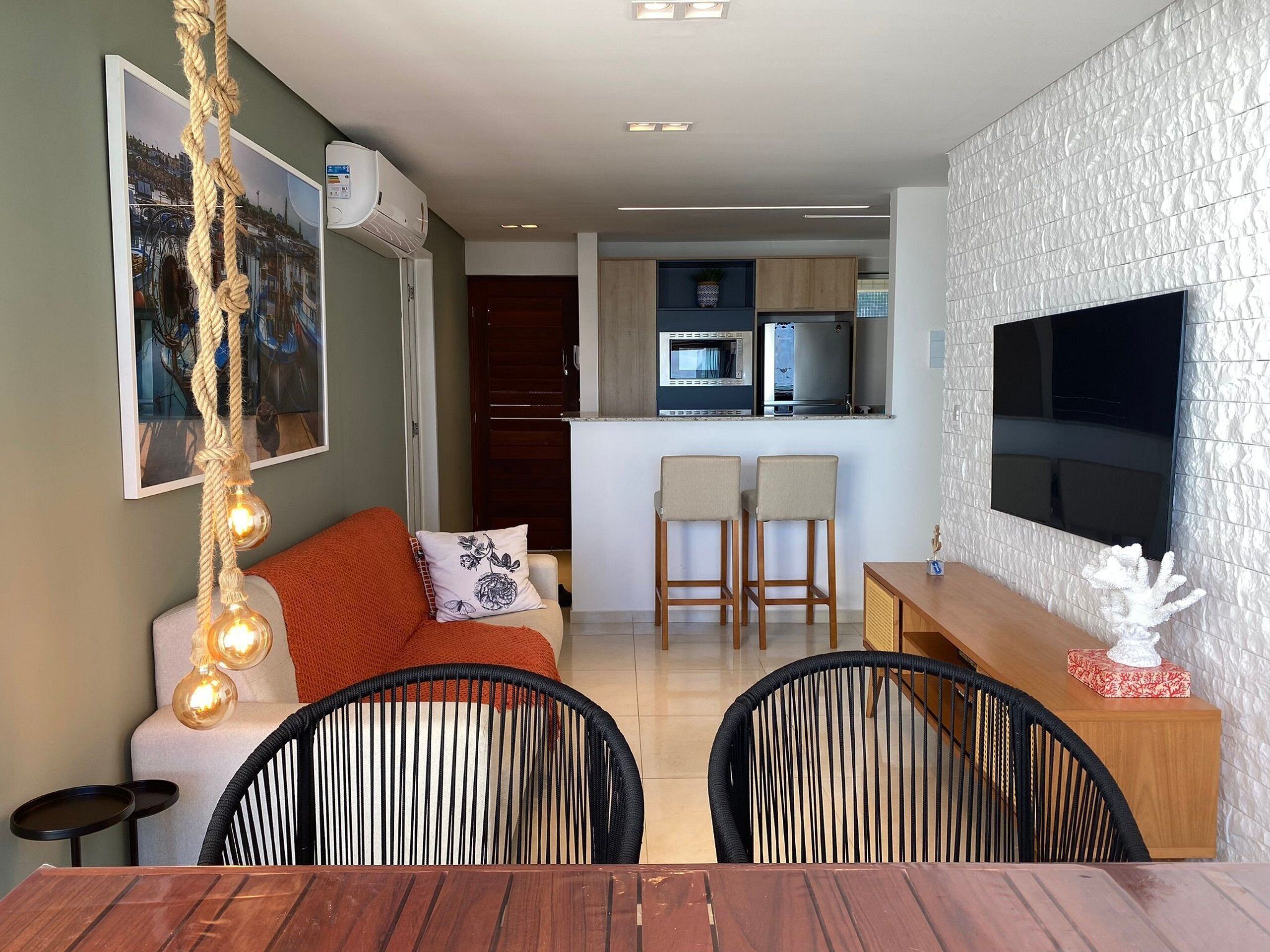 A modern living room with a sofa, two chairs, a dining table, a TV, and a kitchen in the background.