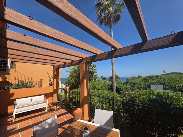 Eine Holz-Pergola mit einer Bank und einem Tisch, mit Blick auf eine üppige grüne Landschaft und das Meer.
