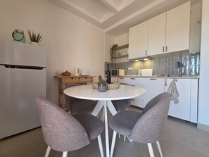 Eine moderne Küche mit weißen Schränken, einem runden Esstisch und vier grauen Stühlen.