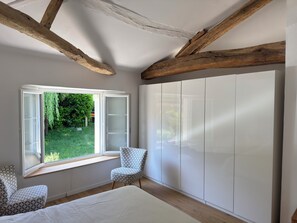 A bedroom with a large wardrobe, a window with a view of greenery, and a patterned chair. - In the quiet of the countryside - Authentic charm - Modern comfort - Air-conditioned (Touvérac)