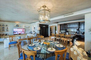 Un comedor amplio con una mesa redonda de vidrio, sillas de madera y una araña.