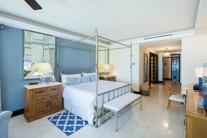 Un dormitorio con cama con dosel, una mesita de noche de madera, un espejo, una mesilla de noche con lámparas y un baño visible a través de una puerta abierta.
