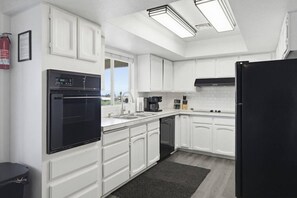 Eine moderne Küche mit weißen Schränken, einem schwarzen Kühlschrank, einem eingebauten Ofen und einer Kaffeemaschine.