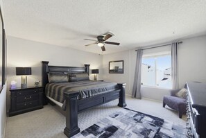 Ein Schlafzimmer mit Bett, Nachttischen, Deckenventilator, Fenster mit Vorhängen und Blick.