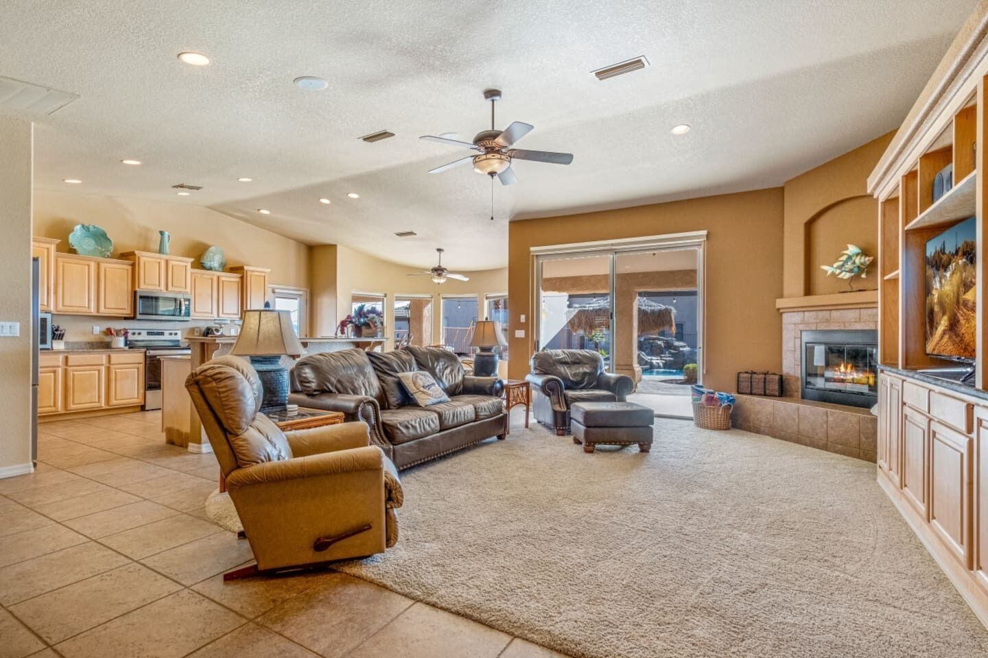 A spacious living area with a fireplace, leather furniture, and a kitchen in the background.