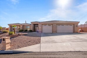 A two-story house with a garage, a driveway, and a small landscaped area with a palm tree.