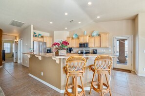 A kitchen with a central island, two barstools, wooden cabinets, and a microwave.