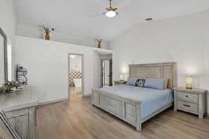 Ein Schlafzimmer mit Bett, Nachttischen, Deckenventilator und Blick ins Badezimmer.
