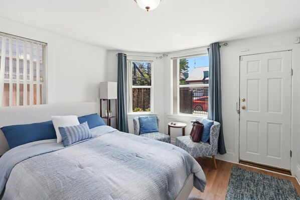 Une chambre à coucher avec un grand lit, deux tables de chevet, une chaise, une armoire et une fenêtre avec des rideaux.