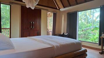 Quarto com uma cama grande, vigas de madeira no teto, vista para o verde e uma porta de madeira.