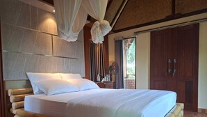 Una cama con sábanas blancas, un ventilador y vistas al exterior.