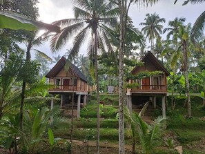 Two wooden cabins with balconies, surrounded by lush greenery and palm trees.