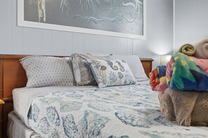 A bedroom with a bed, pillows, a blanket, and a wall painting.