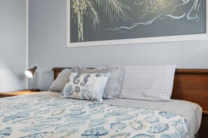 Un dormitorio con cama, almohadas, una mesita de noche, una lámpara y un cuadro en la pared.