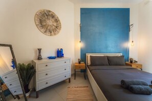 A bedroom with a bed, dresser, bedside tables, a mirror, and a blue accent wall. - Stylish Apartment | 1BR Near Sliema & Valletta (Gżira)