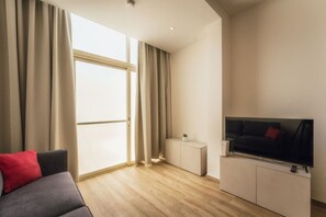 A modern living room with a sofa, a TV, a small side table, and a sliding glass door. - Seafront Gozo Escape | BBQ Backyard by Qbajjar Bay (Gozo)