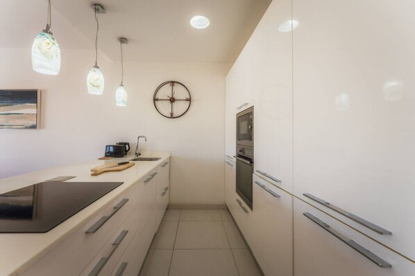 A modern kitchen with a built-in oven, microwave, and a clock on the wall. - Modern Apt in Marsaskala | Near Seafront & Beaches (Marsaskala)