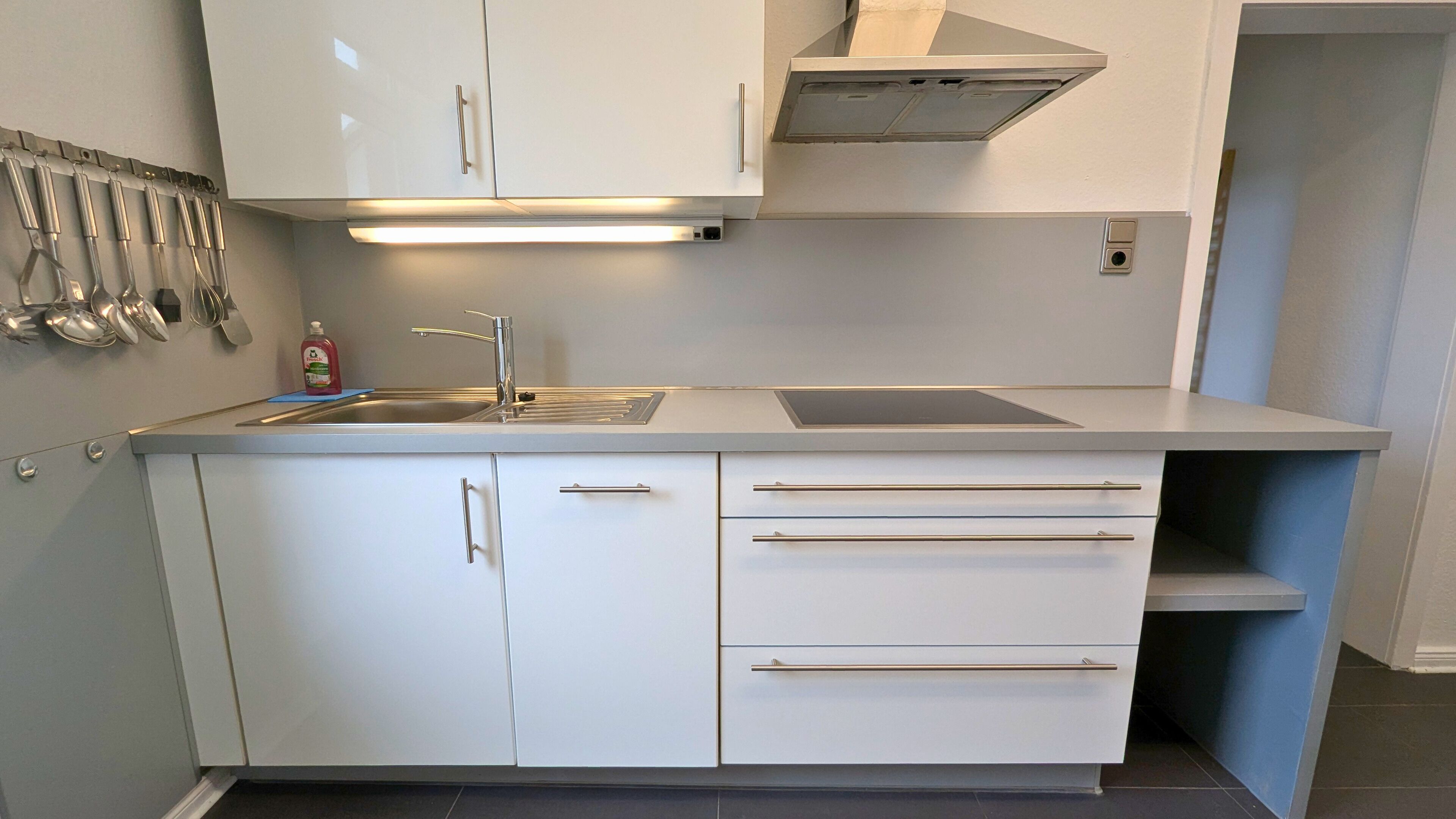 A kitchen with white cabinets, a stainless steel sink, and a range hood.