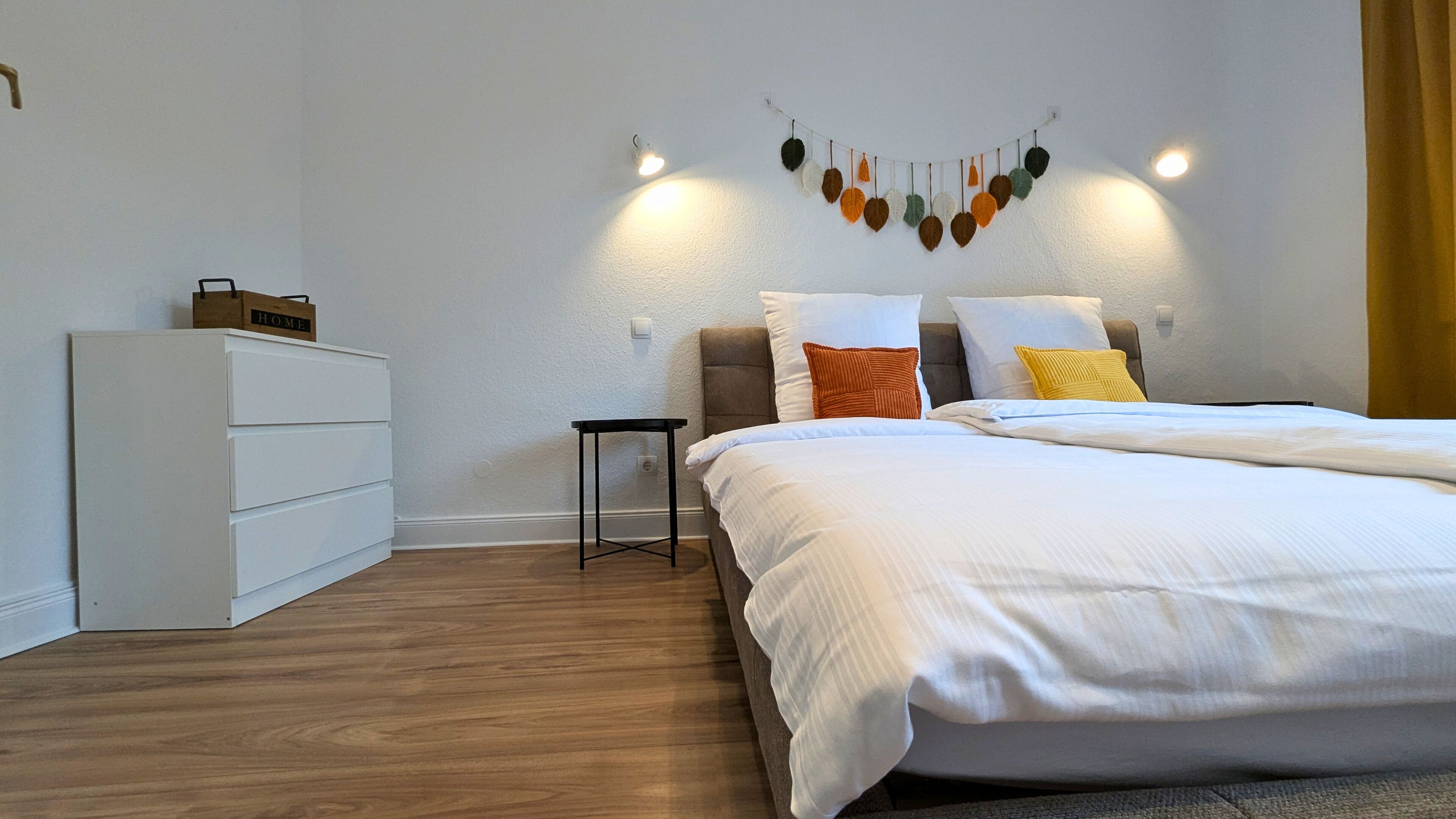 A bedroom with a bed, a dresser, a nightstand, and a wall-mounted light fixture.
