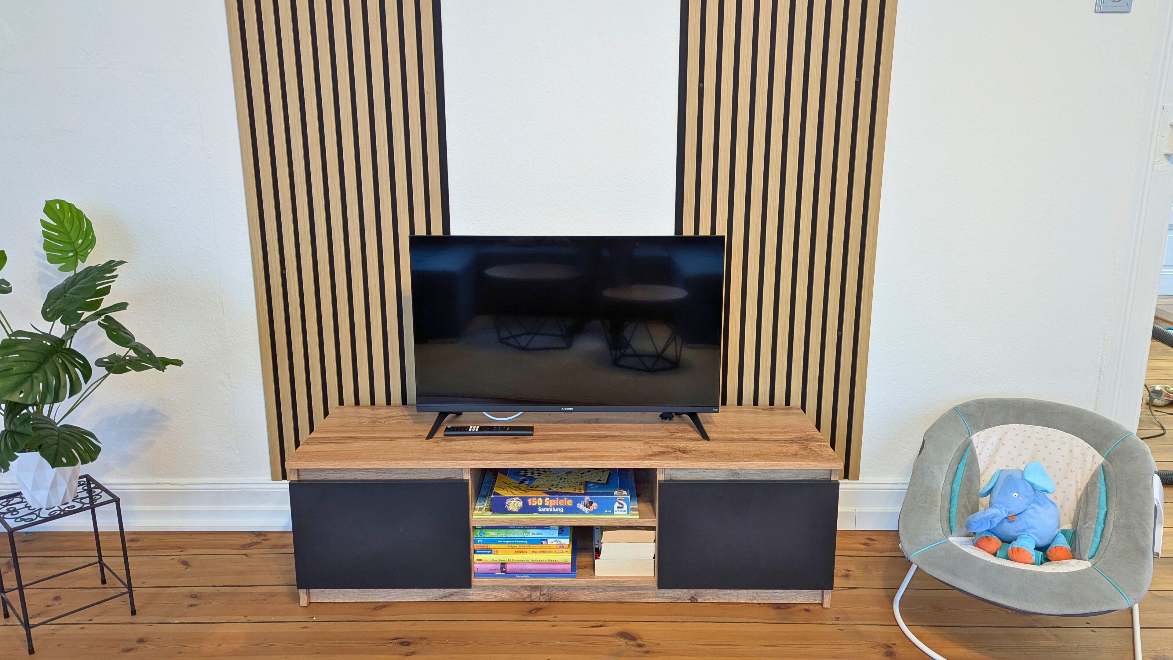 A modern living room with a flat-screen TV, wooden paneling, a bookshelf, and a plush chair.