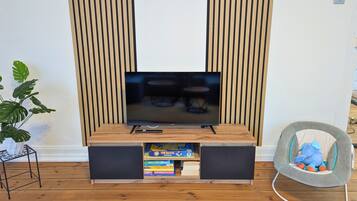 A modern living room with a flat-screen TV, wooden paneling, a bookshelf, and a plush chair.