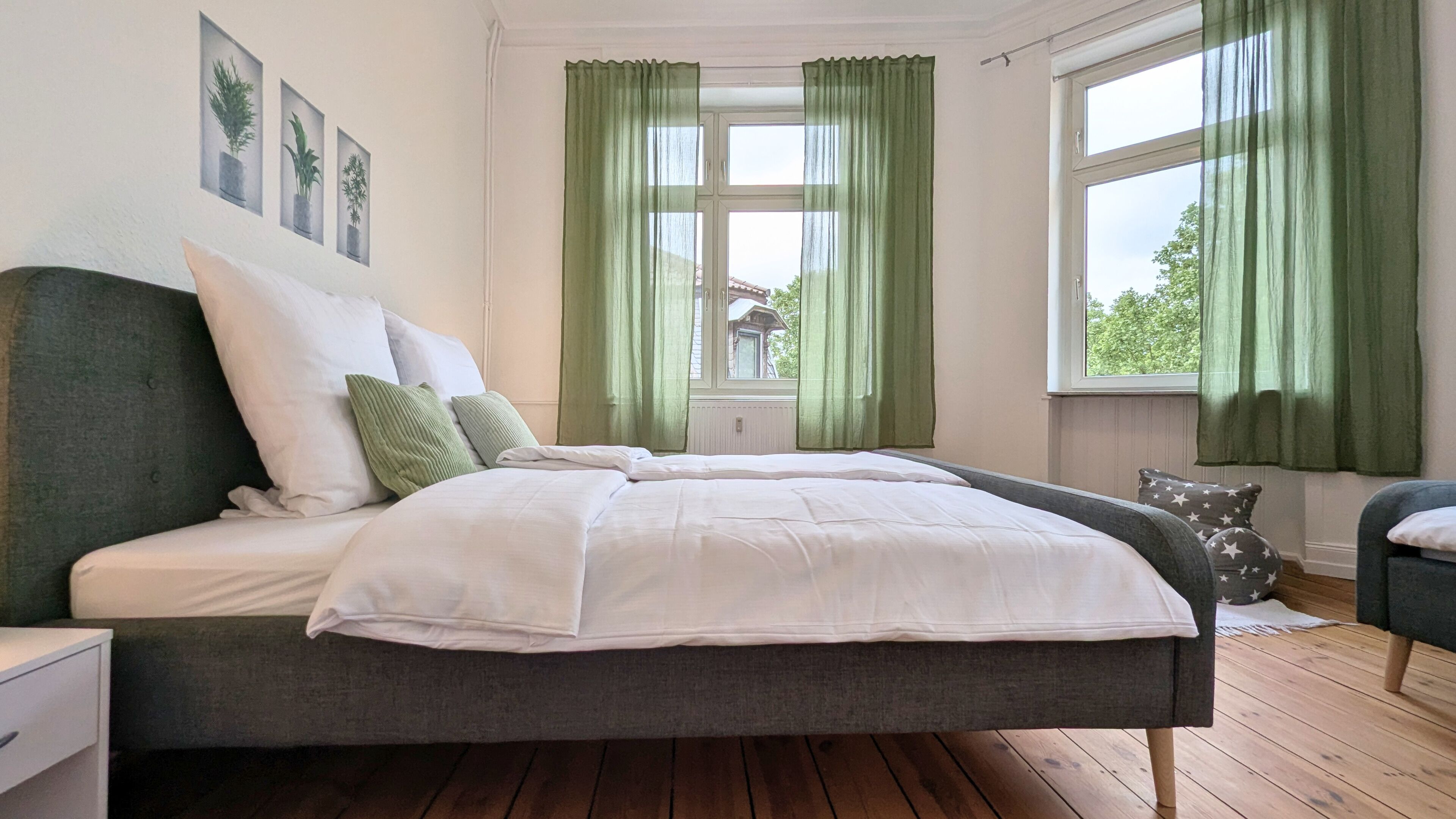 Ein Schlafzimmer mit einem Bett, grünen Vorhängen, einem Fenster und Blick auf ein Haus.