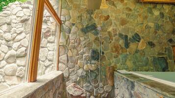 A stone shower enclosure with a rain showerhead and a handheld showerhead.